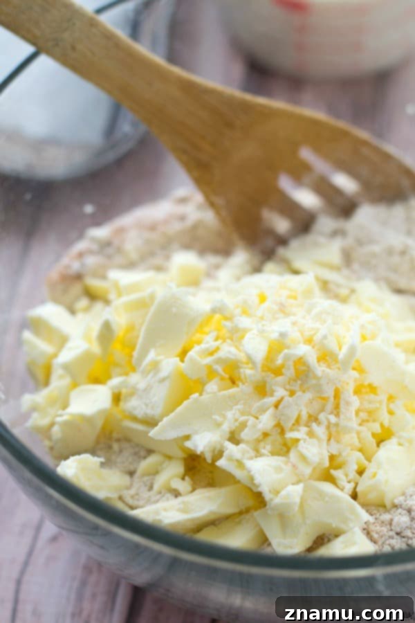 Cubed, ice-cold butter being added to the dry flour mixture, essential for creating flaky buttermilk biscuits.