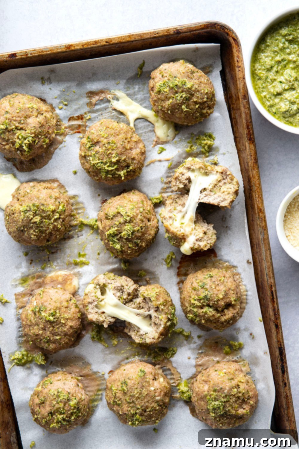 Melted Mozzarella Pesto Turkey Meatballs 2 Close-up of baked mozzarella-stuffed pesto turkey meatballs on a sheet pan, garnished with fresh basil.