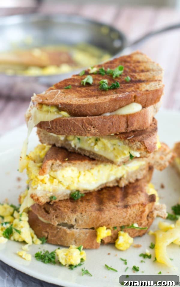 The Scramble Melt 6 A hand holding a half of a Scrambled Egg Grilled Cheese sandwich with cheese stretching