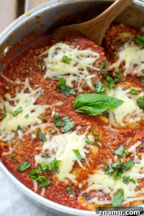 30-Minute One-Pan Chicken Parmesan 4 Fresh basil leaves garnish a succulent piece of chicken parmesan, featuring a golden-brown crust, rich red sauce, and luscious melted cheese.