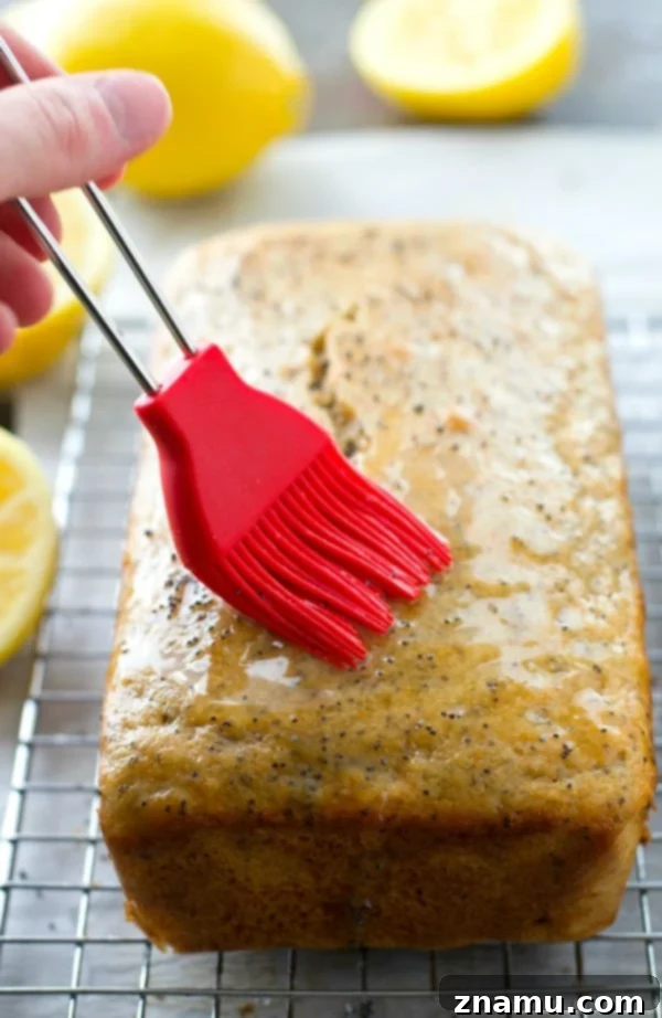Zesty Poppy Drizzle Loaf 7 A loaf of freshly baked Lemon Poppy Seed Bread, warm from the oven, being brushed with a lemon soaking syrup.