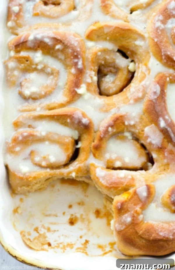 Decadent Orange Cinnamon Roll with Icing A close-up of a single orange cinnamon roll, showcasing its fluffy texture and generous layer of cream cheese icing.