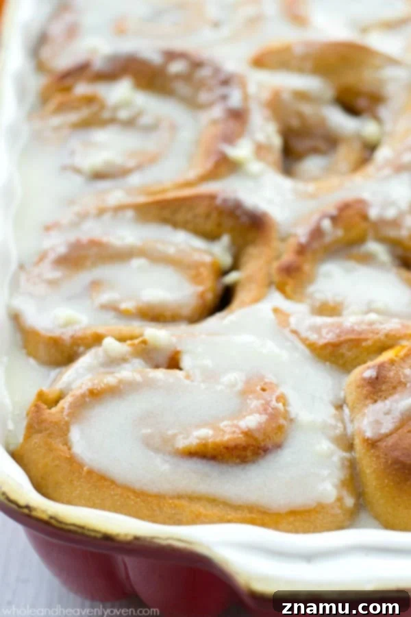 Two Orange Cinnamon Rolls, Ready to Enjoy A plate featuring two freshly baked orange cinnamon rolls, adorned with a generous dollop of cream cheese icing, perfect for breakfast.