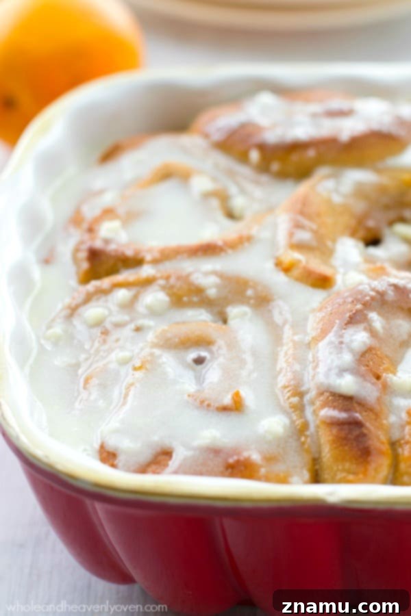 Cream Cheese Icing on Warm Orange Cinnamon Rolls A close-up of several orange cinnamon rolls arranged in a baking dish, generously covered with a smooth cream cheese icing.