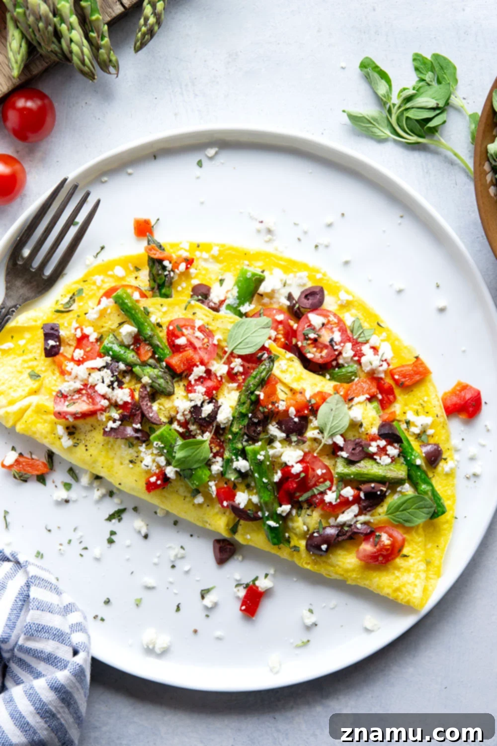 Mediterranean Asparagus & Feta Omelet 2 A perfectly cooked Greek omelet overflowing with vibrant green asparagus, bright red cherry tomatoes, and crumbled white feta cheese, ready to be served on a pristine white plate.