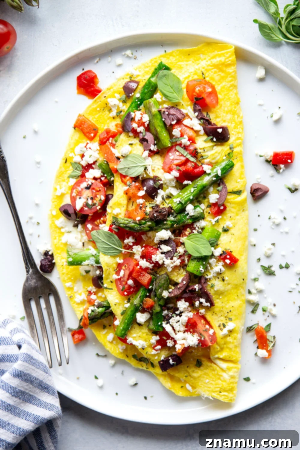 Mediterranean Asparagus & Feta Omelet 6 Two freshly cooked Greek omelets on white plates, garnished with extra cherry tomatoes, asparagus, and feta, highlighting their readiness to be enjoyed.