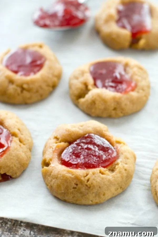 Buttery Shortbread Jam Impressions 3 Close-up of freshly baked jam shortbread thumbprint cookies, showing their golden edges and glistening jam centers.