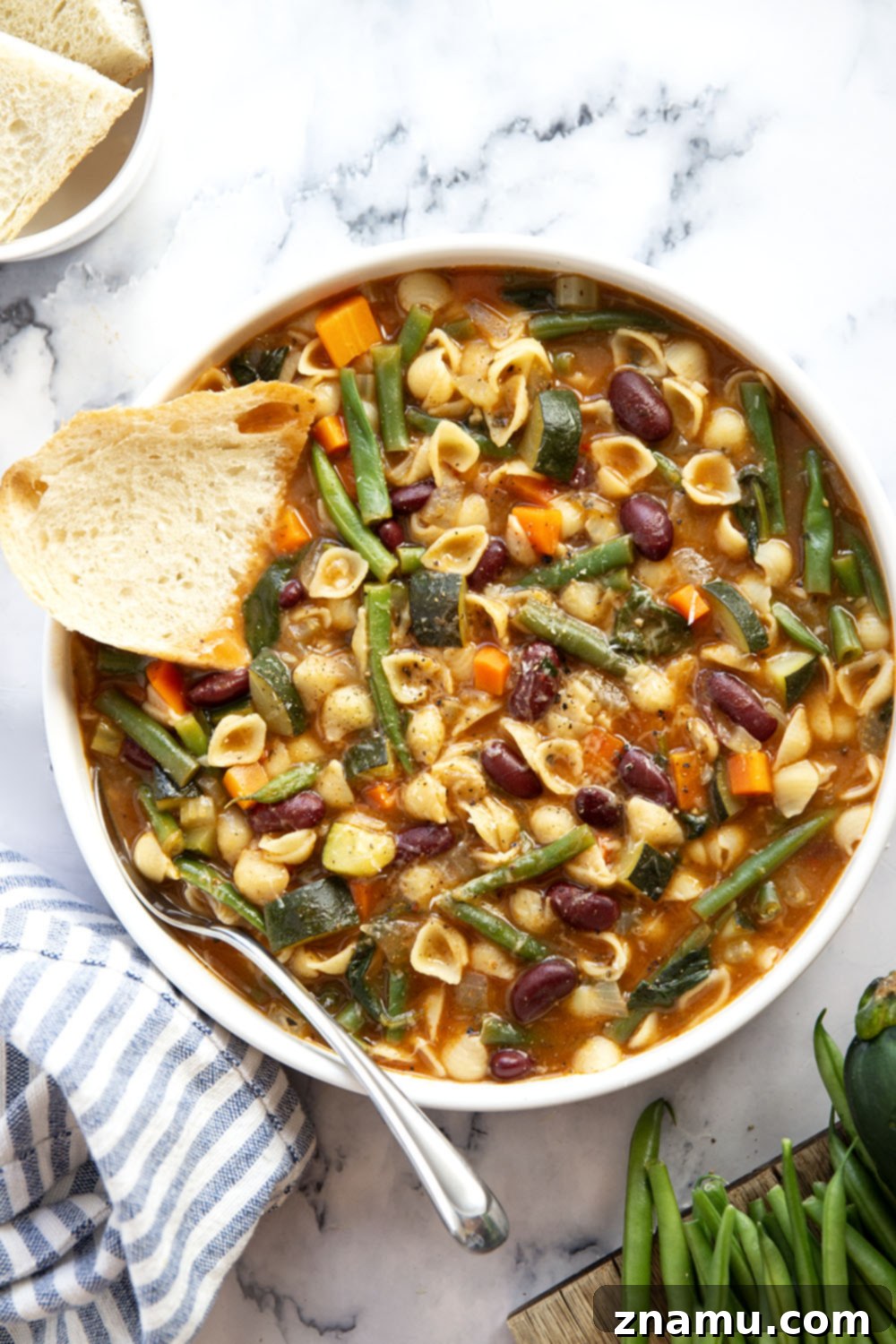 Hearty Vegetarian Minestrone 6 Overhead shot of two bowls of vegetarian minestrone soup, garnished with fresh basil and grated cheese, on a rustic wooden surface.