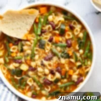 A vibrant, hearty bowl of vegetarian minestrone soup with fresh vegetables, beans, and pasta, garnished with fresh herbs and Parmesan.