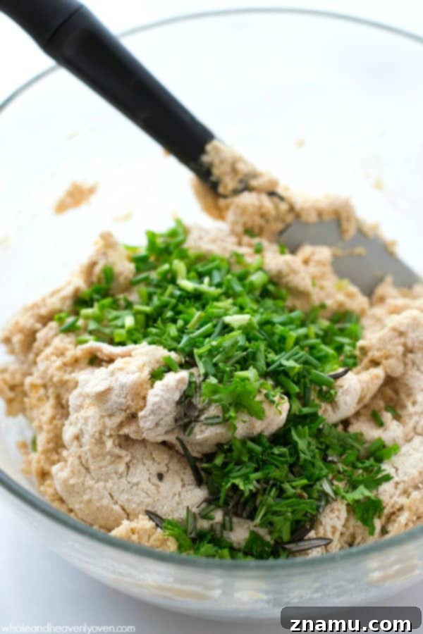 A bowl of biscuit dough, visibly studded with green fresh herbs and Parmesan cheese, ready for shaping.