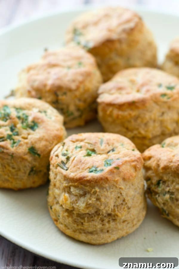 A batch of golden-brown Herbed Greek Yogurt Buttermilk Biscuits resting on parchment paper after baking, brushed with butter.