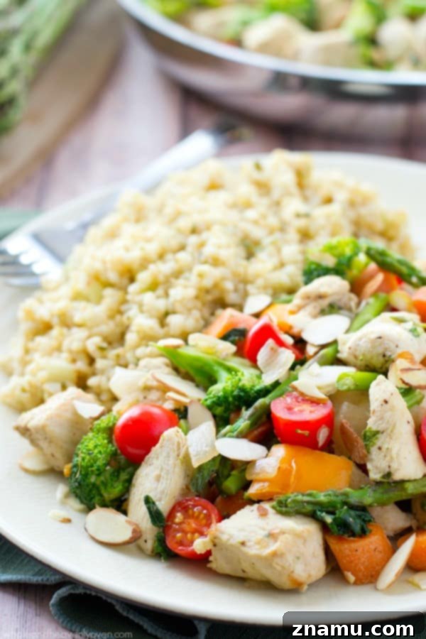 Chicken Asparagus Stir-Fry with Sweet Tomatoes and Crunchy Almonds 4 A large skillet filled with cooked chicken, asparagus, cherry tomatoes, and other spring vegetables, ready to be served over rice.