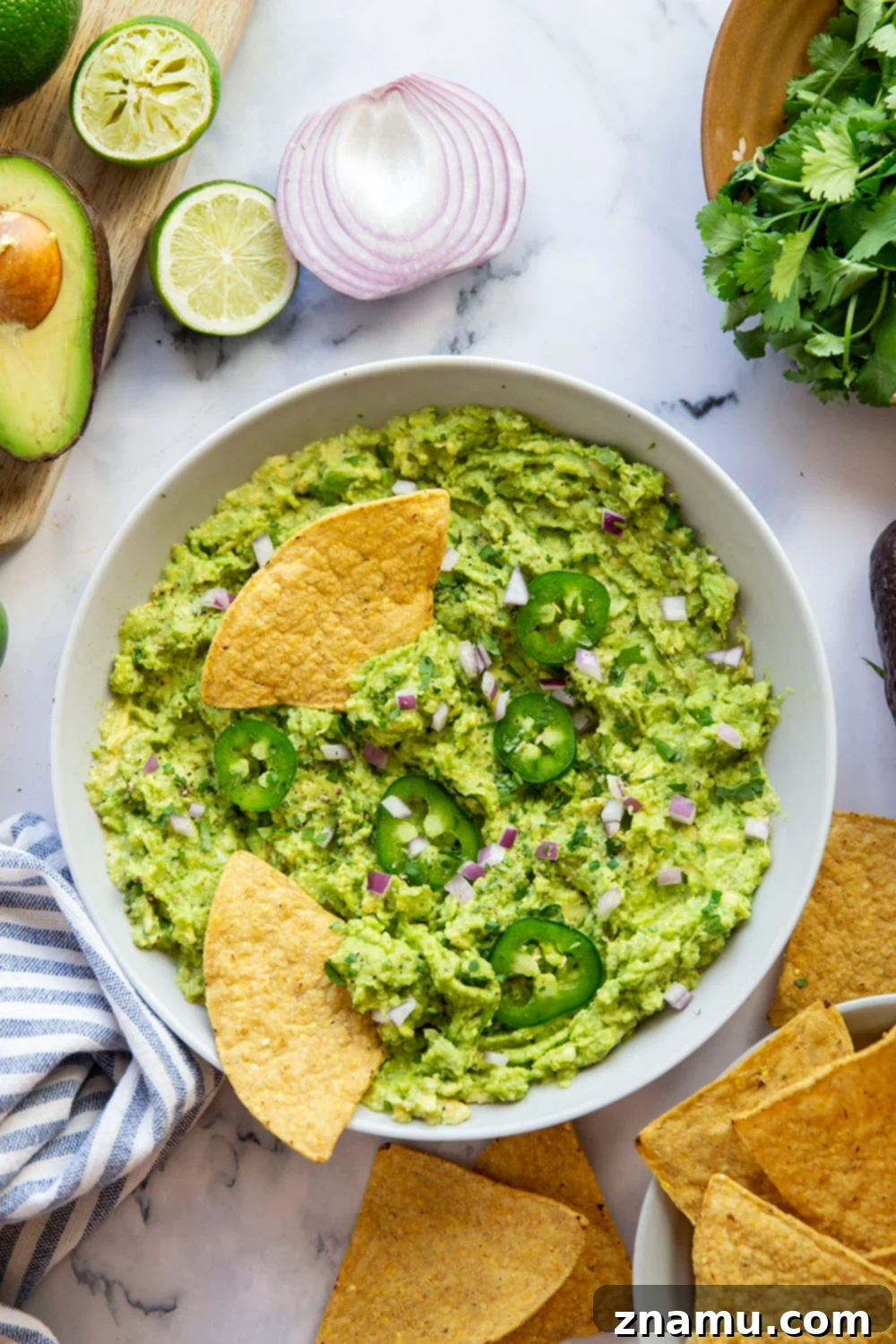 The Ultimate Guacamole Recipe 5 Several ripe avocados on a wooden cutting board, with one cut open to reveal the pit and creamy flesh.