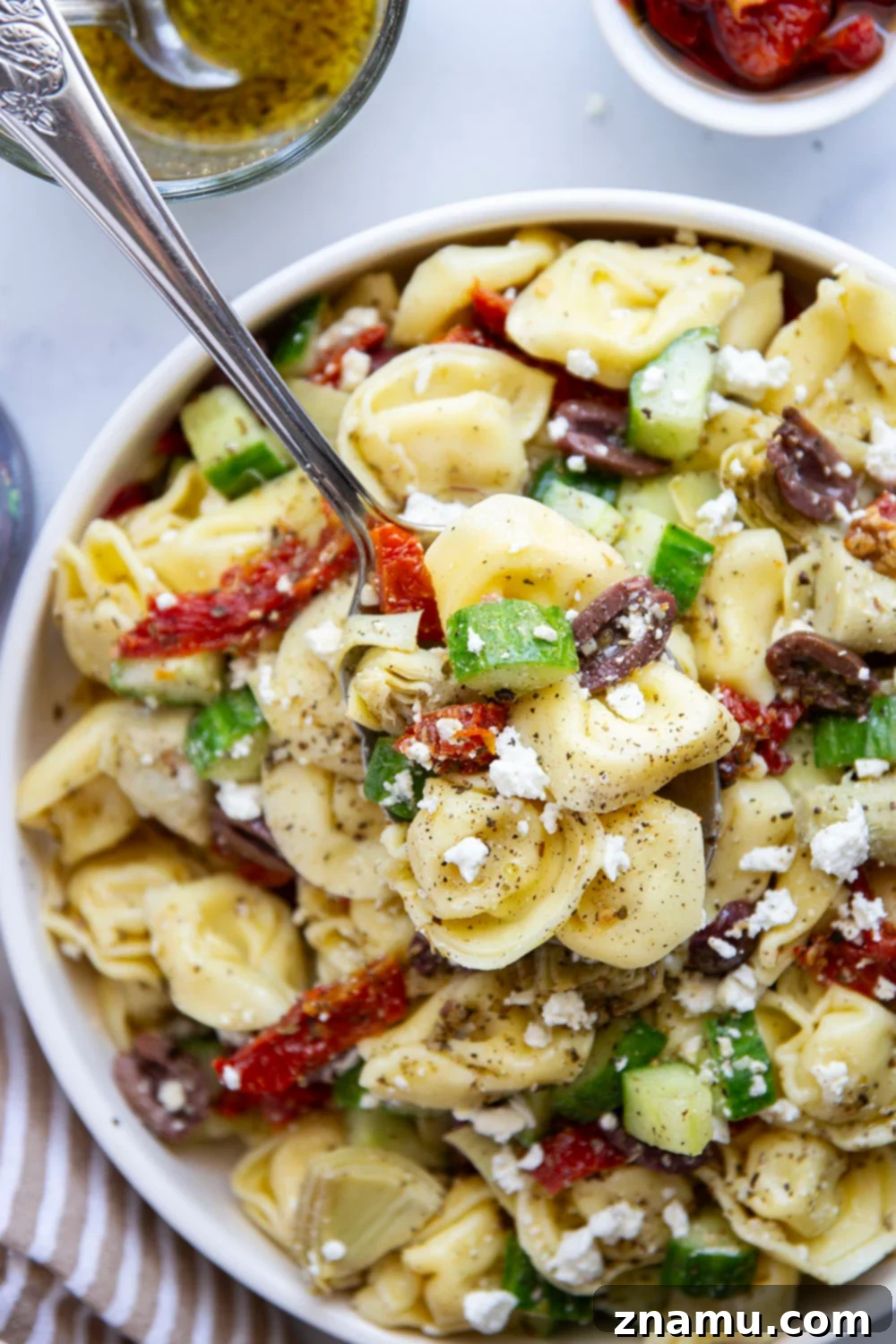 Vibrant Mediterranean Tortellini Pasta Salad 6 Serving bowl of Mediterranean tortellini pasta salad with a spoon.