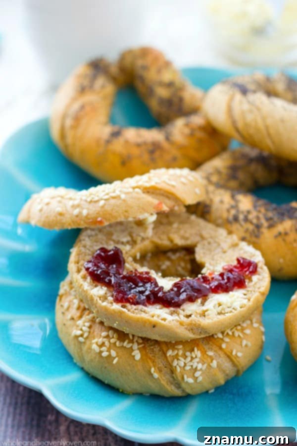 Authentic Homemade Deli Bagels 10 Several homemade bagels with sesame seeds are arranged on a parchment-lined baking sheet, freshly baked and ready to be removed from the oven.