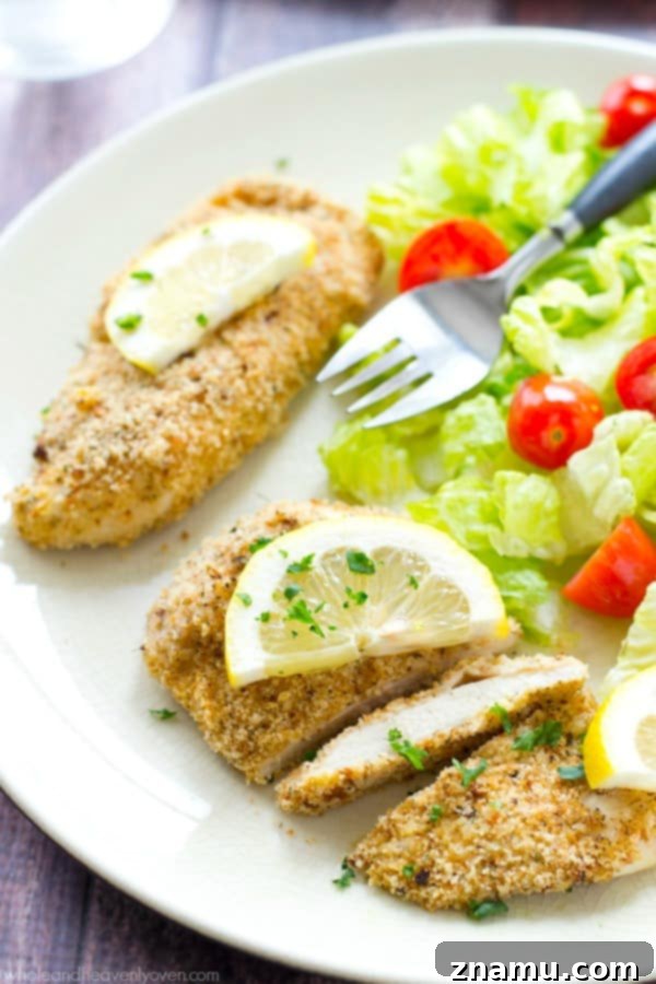 Irresistible Lemon-Garlic Crusted Chicken Tenders 7 A hand reaching for a piece of the crispy lemon-garlic chicken tender from a serving platter.