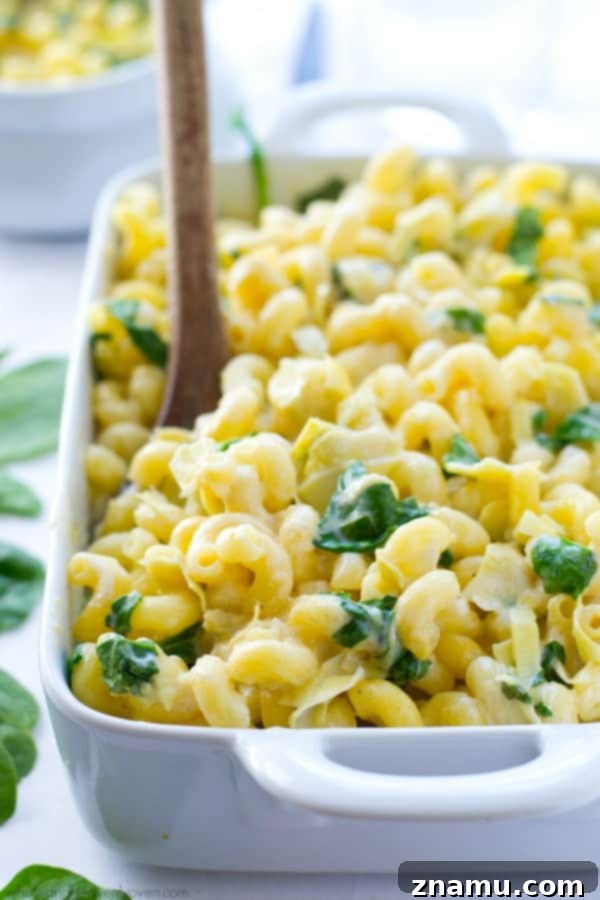 Creamy Spinach Artichoke Mac n Cheese 7 Generous serving of Spinach Artichoke Mac and Cheese being scooped from a pan