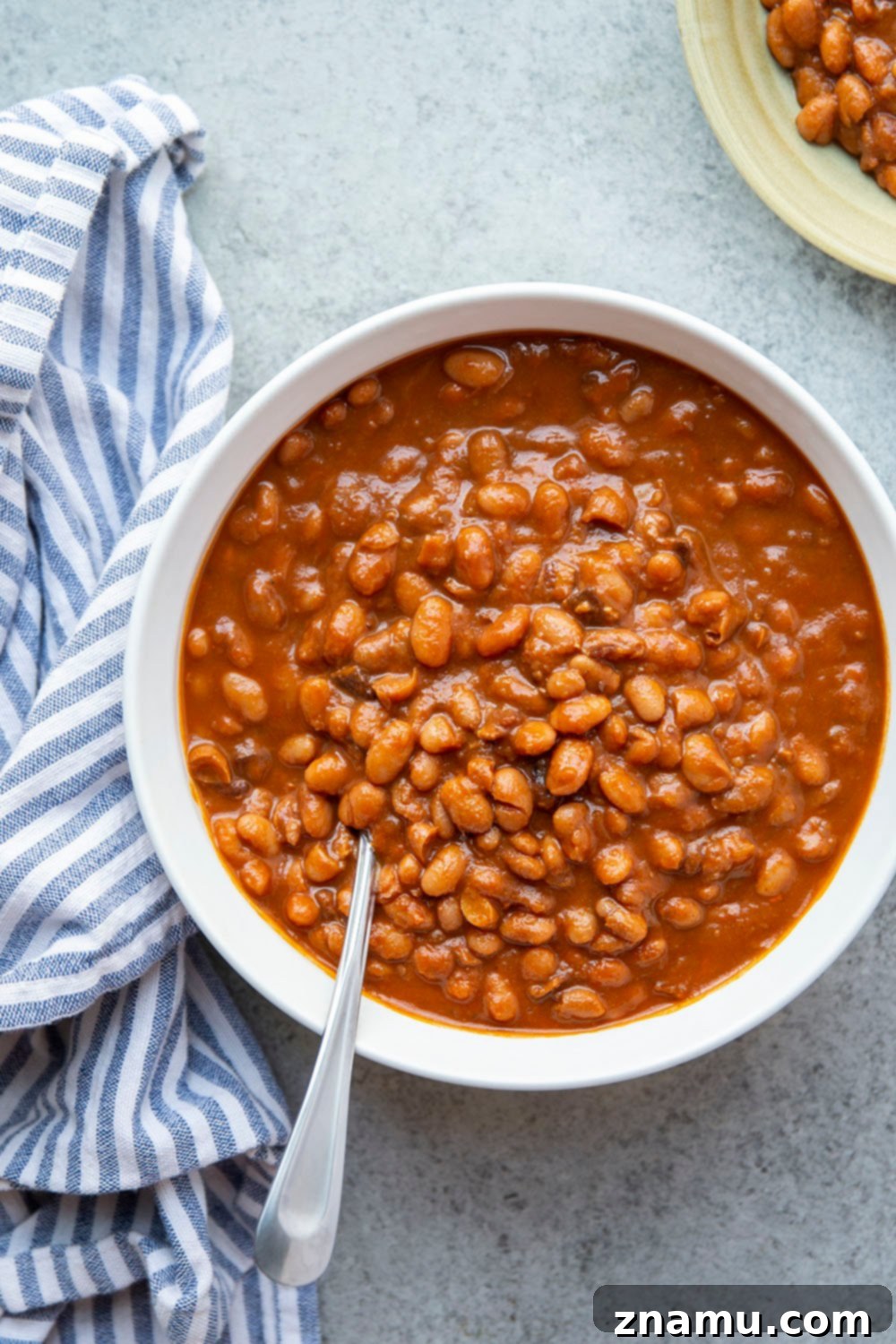 A close-up of tender, smoky homemade slow cooker baked beans, ready to be served at a family cookout.