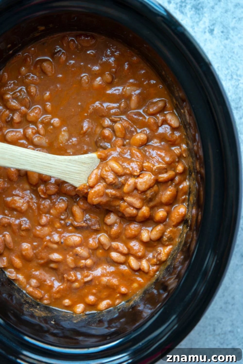 Overhead view of slow cooker baked beans in a serving dish, garnished with fresh parsley.