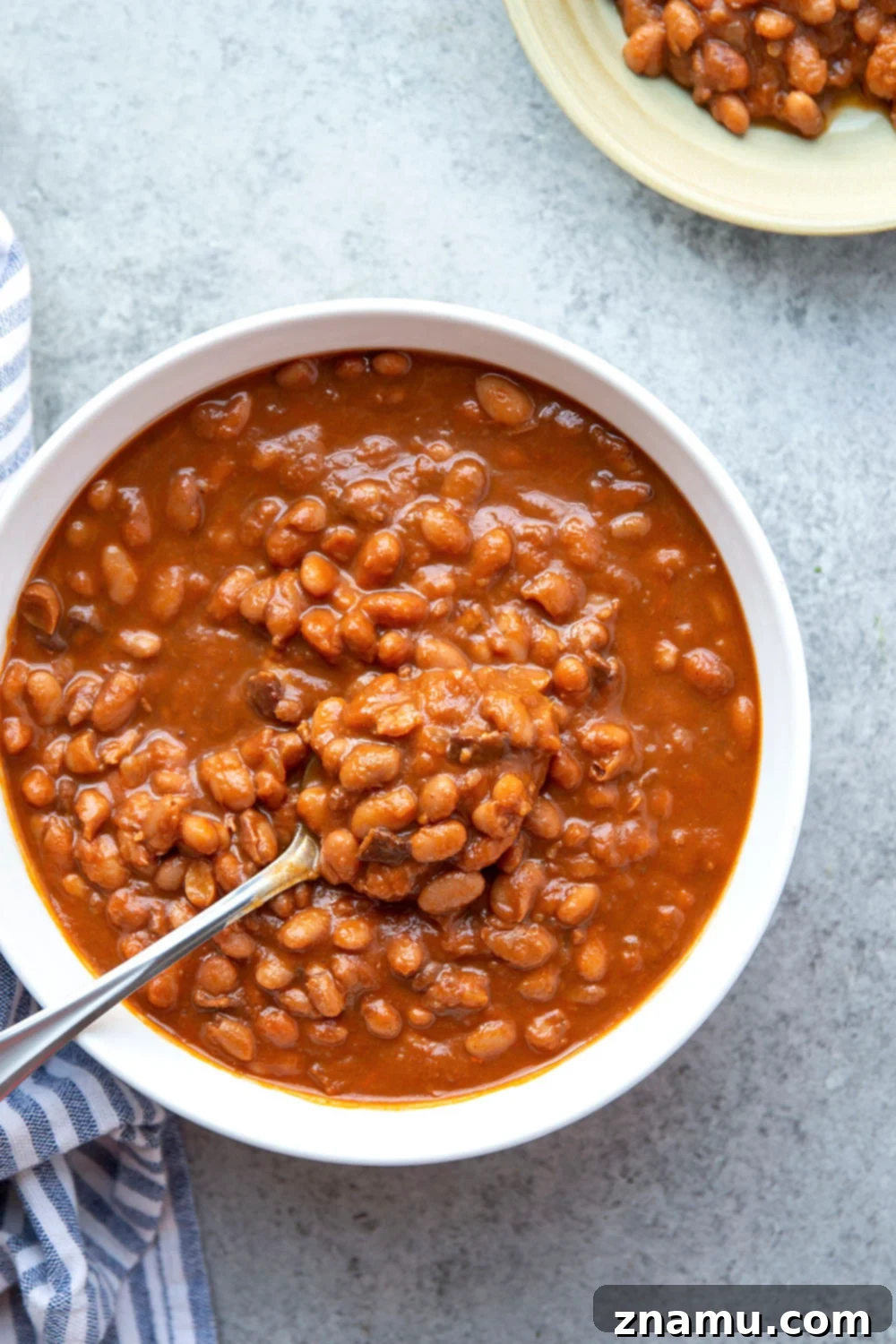 Ingredients for slow cooker baked beans laid out on a wooden cutting board, including beans, bacon, onions, and spices.