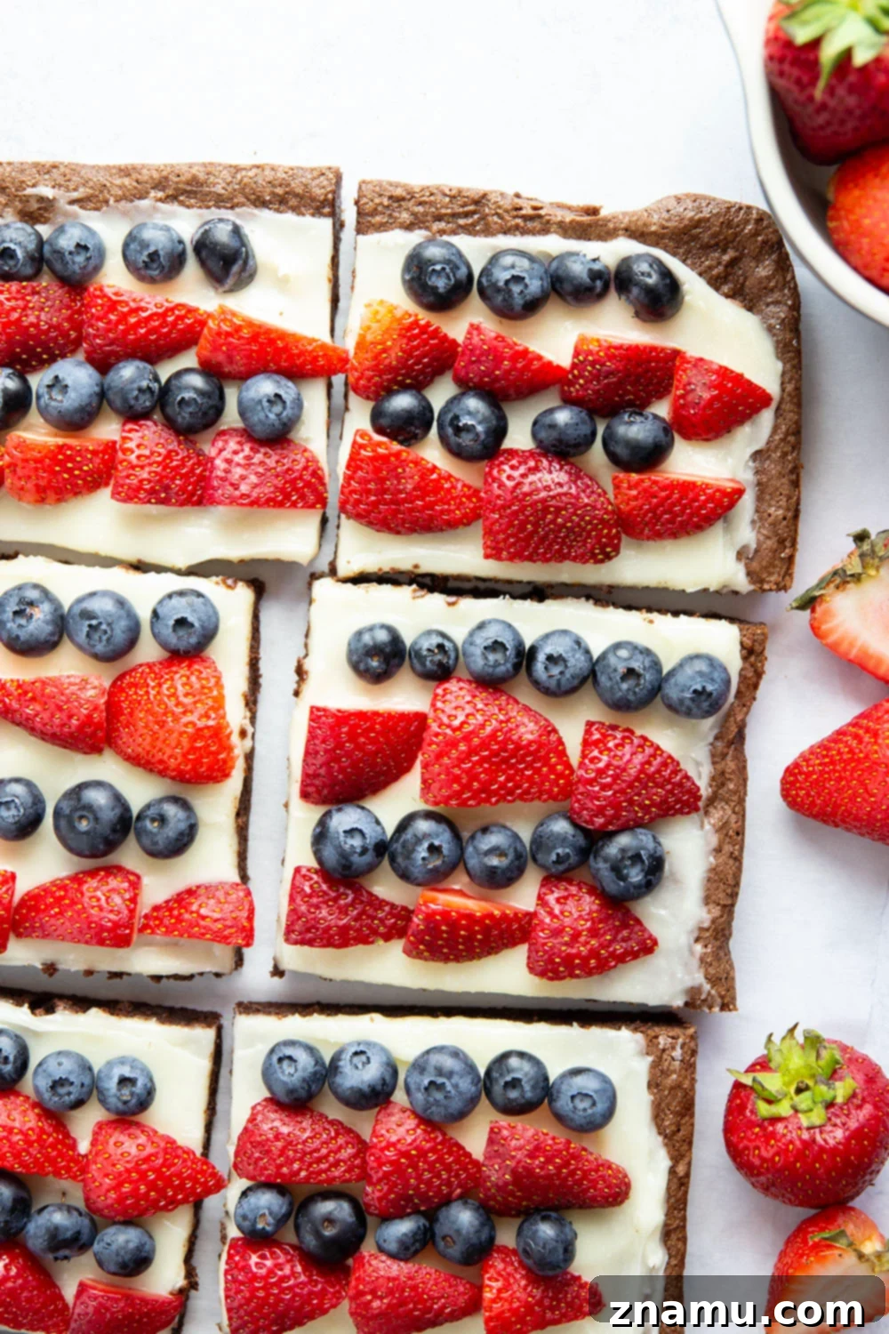 Red, White & Blue Brownie Pizza 2 A festive 4th of July brownie dessert pizza, featuring a rich chocolate brownie base, creamy white frosting, and a vibrant topping of red strawberries and blue blueberries arranged in a flag-like pattern.