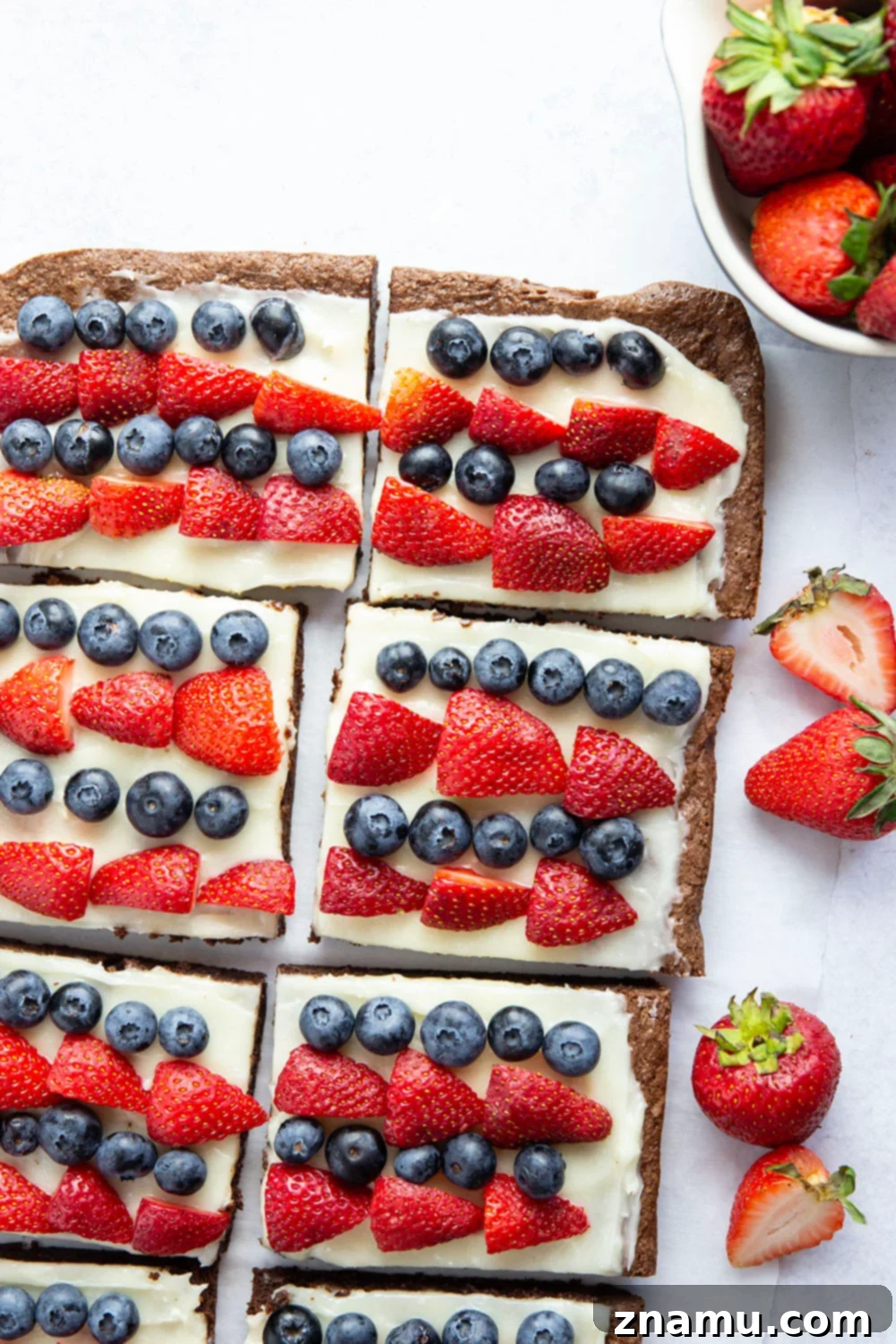 Red, White & Blue Brownie Pizza 5 A close-up of a square piece of the 4th of July brownie dessert pizza, showing the thick brownie base, white cream cheese frosting, and perfectly aligned rows of red strawberries and blue blueberries.