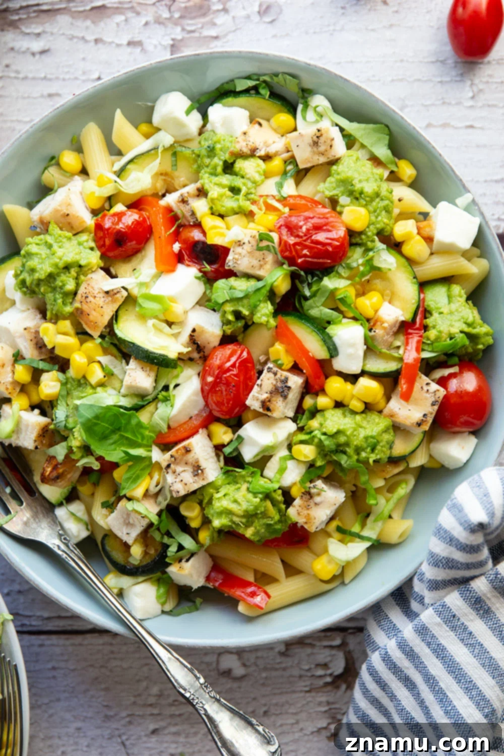 Close-up of a colorful California grilled chicken vegetable pasta bowl with avocado, corn, and basil