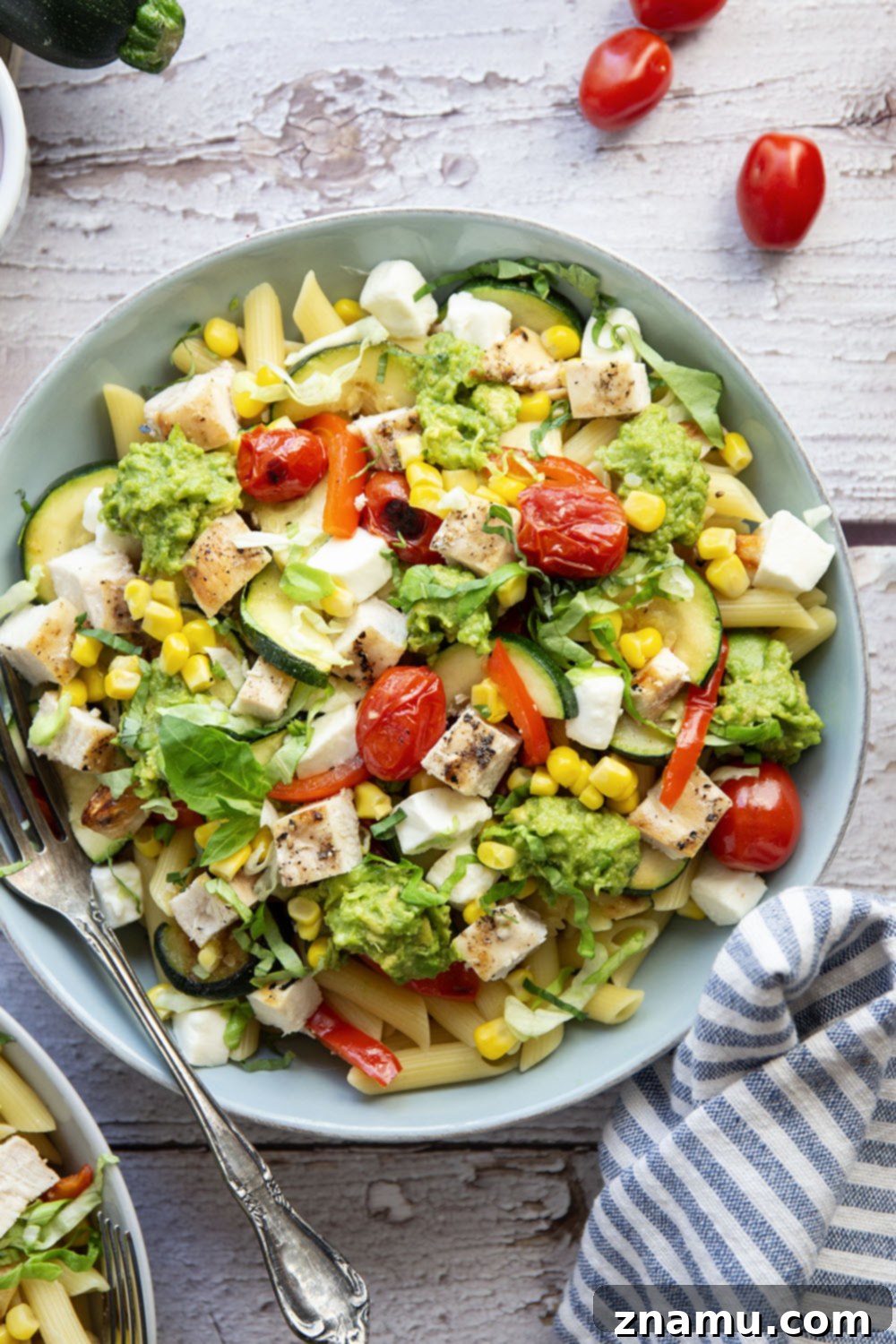 Close-up of a completed California grilled chicken vegetable pasta bowl with fresh basil