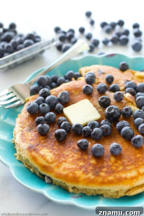 Colossal Buttermilk Blueberry Pancake 4 An XXL blueberry buttermilk pancake on a plate, ready to be enjoyed, emphasizing its impressive size.
