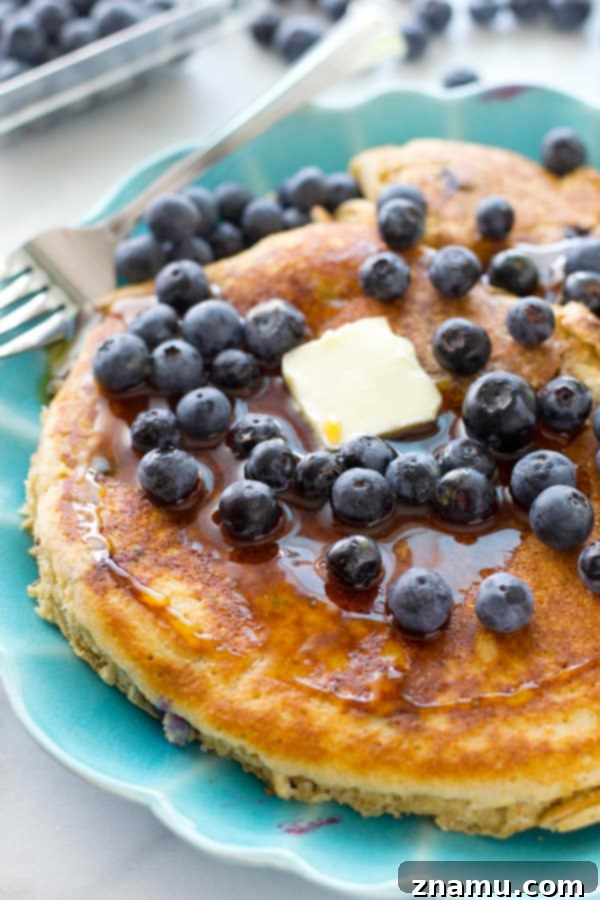 Colossal Buttermilk Blueberry Pancake 7 A close-up of a giant blueberry buttermilk pancake being drizzled with rich maple syrup.