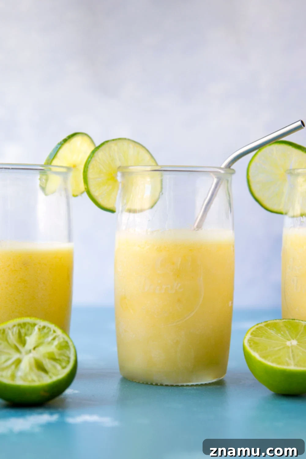 Tropical Pineapple Margarita Slush 4 Overhead shot of two pineapple margarita slushies, one garnished with lime and pineapple wedge, on a wooden surface