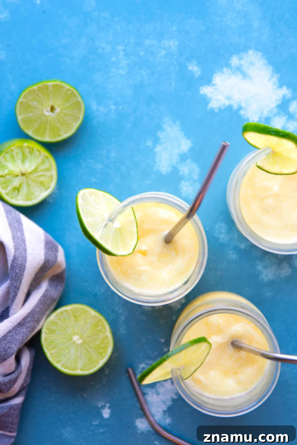 Tropical Pineapple Margarita Slush 5 A hand holding a clear glass of pineapple margarita slushy, topped with a lime wedge