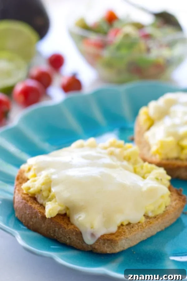 Cheesy Scramble Toast with Fresh Avocado and Burst Tomatoes 6 Close-up of fluffy scrambled eggs with melted cheese on toast, topped with a fresh avocado cherry tomato medley, ready to be enjoyed.