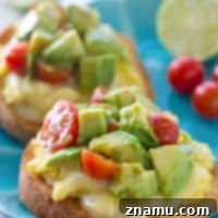 Close-up of avocado cherry tomato medley on cheesy scrambled egg toast, showcasing the fresh toppings.