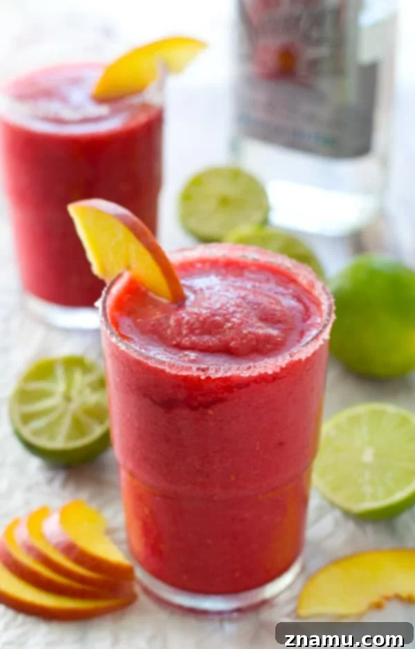Frozen Raspberry Peach Cocktail Bliss 2 A tall glass filled with a bright pink raspberry peach slushie, garnished with fresh raspberries and a lime wedge, sitting on a rustic wooden surface, exuding a refreshing summery vibe. Ideal for quick summer cocktails.