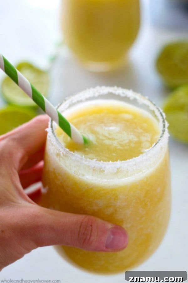Frozen Raspberry Peach Cocktail Bliss 11 A tall glass filled with icy-cold tropical pineapple margarita slushie, garnished with a pineapple wedge and lime, suggesting a refreshing escape to the tropics.