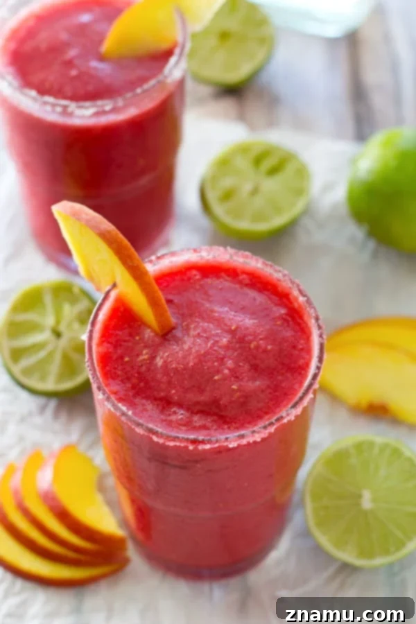 Frozen Raspberry Peach Cocktail Bliss 3 Close-up shot of two glasses of raspberry peach slushies, showcasing the icy texture and colorful layers, garnished with fresh fruit, set against a blurred outdoor background, perfect for a summer gathering.