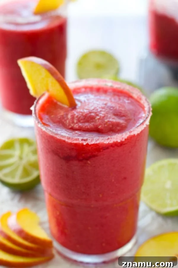 Frozen Raspberry Peach Cocktail Bliss 4 A pitcher full of freshly blended raspberry peach slushie, ready to be poured, with a backdrop of colorful ingredients and preparation tools, emphasizing freshness and homemade quality.
