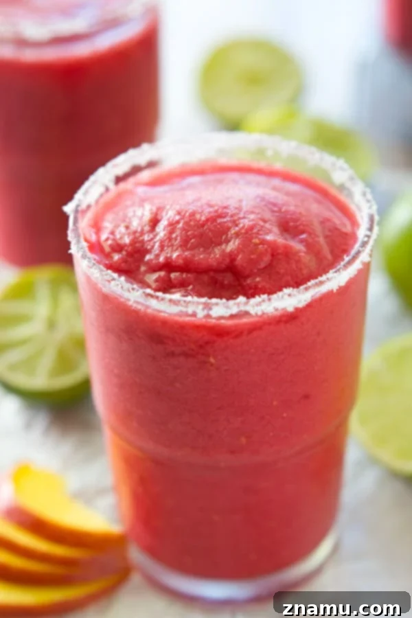 Frozen Raspberry Peach Cocktail Bliss 5 A vibrant raspberry peach slushie in a stemmed glass, adorned with a slice of peach and fresh raspberries, set against a soft-focus background, suggesting a luxurious yet easy summer treat.