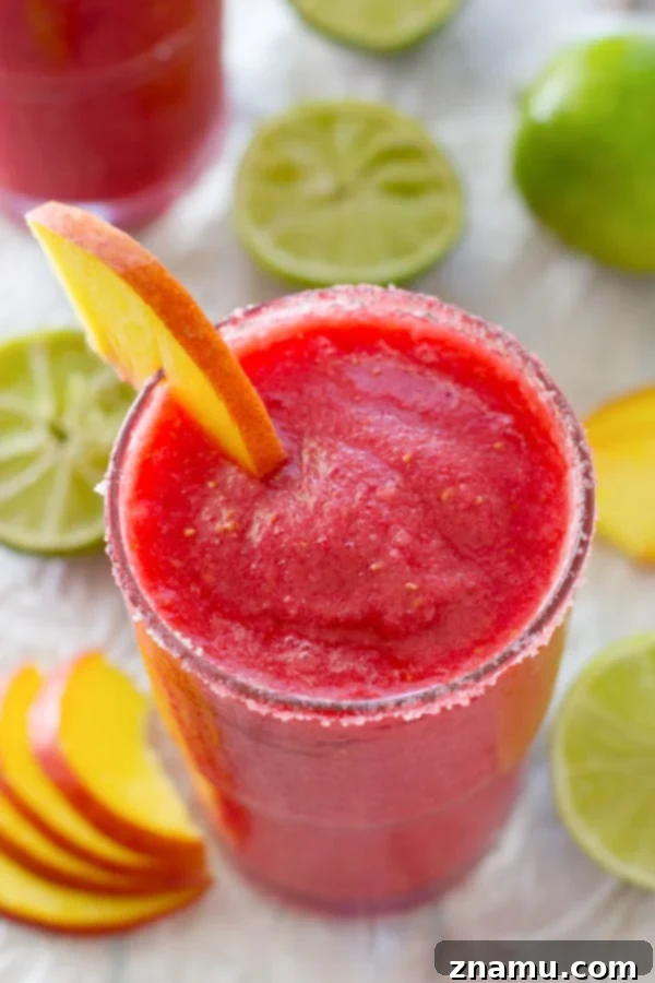 Frozen Raspberry Peach Cocktail Bliss 6 A hand holding a tall glass of raspberry peach slushie, showing its perfect icy consistency and appealing color, with a festive straw, inviting immediate enjoyment.