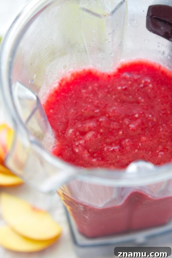 Frozen Raspberry Peach Cocktail Bliss 8 A close-up of a raspberry peach slushie being poured from a blender into a tall, salt-rimmed glass, emphasizing the smooth, thick texture and the vibrant color of the cocktail.