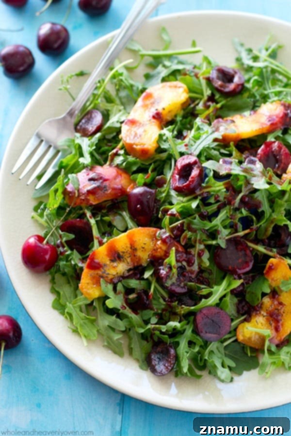 A vibrant grilled peach arugula salad, featuring sweet grilled peach wedges, juicy cherries, and a luscious raspberry balsamic dressing.
