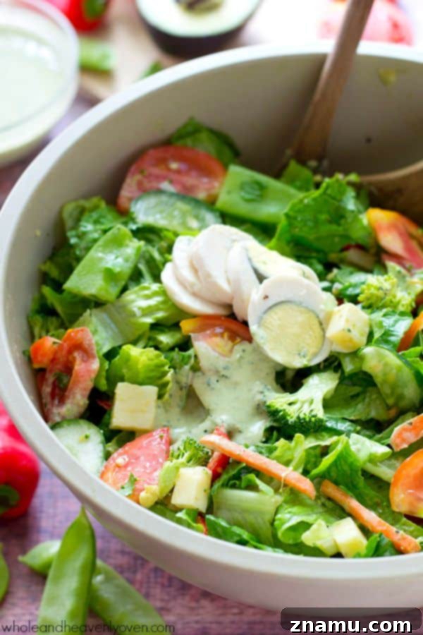 A hand drizzling the creamy pesto ranch dressing generously over the Rainbow Veggie Chef's Salad.