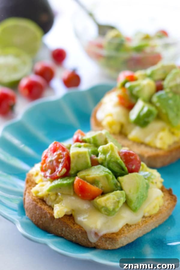 Cali Egg Avocado Toast 12 Enjoy a hearty and delicious cheesy scrambled egg toast, perfectly paired with fresh avocado and a sweet cherry tomato medley for a fulfilling meal.