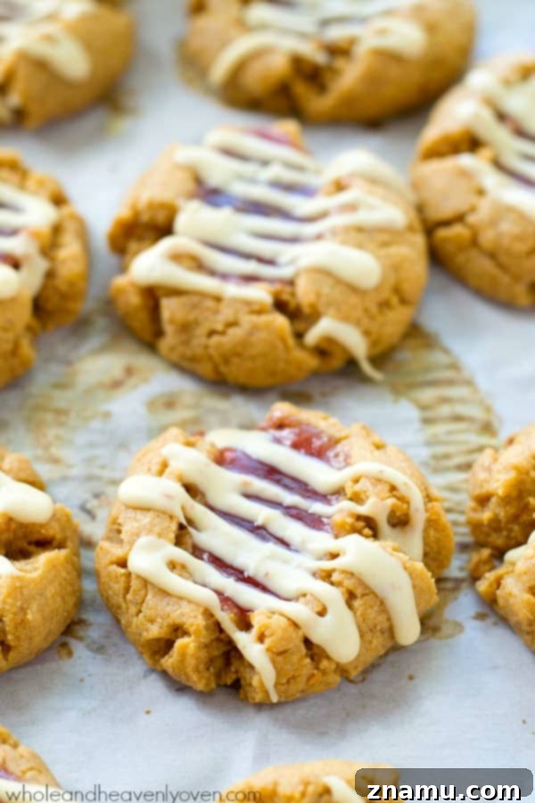 Soft and chewy peanut butter thumbprint cookies filled with fruity jam and drizzled with white chocolate, inviting to be enjoyed with a glass of cold milk.