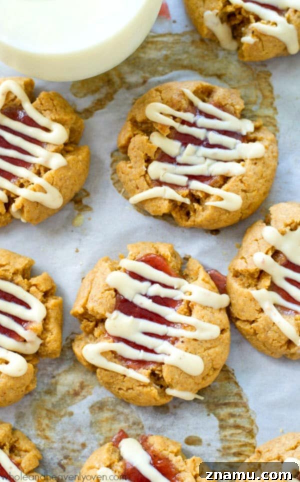 A batch of freshly baked white chocolate peanut butter and jelly thumbprint cookies arranged on a white surface, showcasing their delicious appearance.