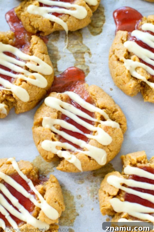 A hand reaching for a white chocolate peanut butter and jelly thumbprint cookie, with the jam filling visible.