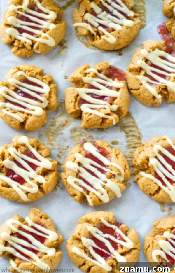 A plate of meticulously arranged white chocolate peanut butter and jelly thumbprint cookies, showing their vibrant jam centers and elegant white chocolate drizzles.