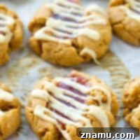 Soft and chewy peanut butter thumbprint cookies filled with fruity jam and drizzled with white chocolate.