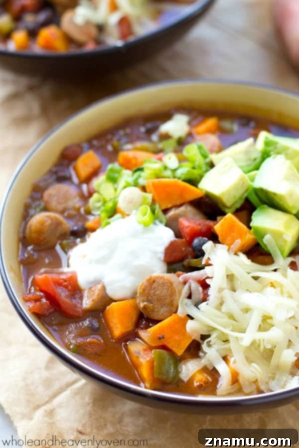 Hearty Slow Cooker Sweet Potato Sausage Chili 4 A serving spoon lifting a scoop of chunky Sweet Potato Sausage Chili from a rustic bowl.